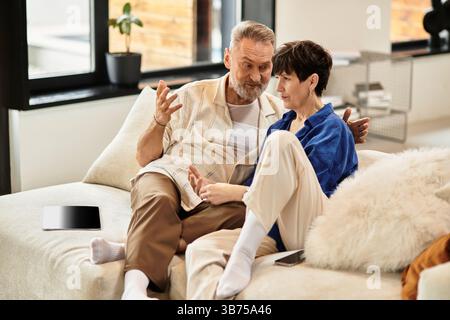 A middle aged man and woman sit closely on a couch, engaged in a lively conversation at home. Stock Photo