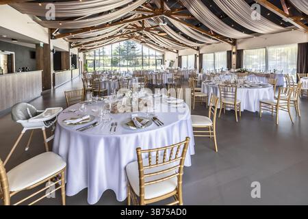 Wedding setting and decorated tables in a beautiful modern interior of a performance hall with a modern light ceiling of wooden construction. Stock Photo