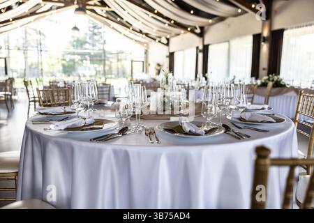 Wedding setting and decorated tables in a beautiful modern interior of a performance hall with a modern light ceiling of wooden construction. Stock Photo