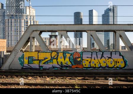 Graffiti on iron train bridge in Manchester with high rise skyscrapers in the background. Northern England, 2025. Stock Photo