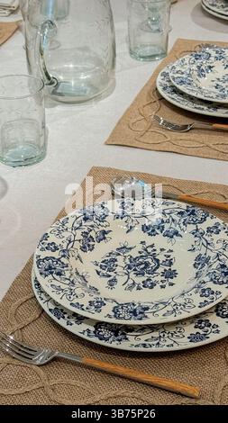 Elegant table setting with blue floral plates, rustic burlap placemats, and glassware creating a charming dining atmosphere. Stock Photo