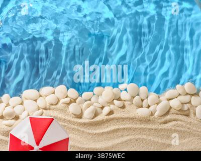 Summer background with sand, white stones, red sun umbrella on edges and blue background sea water with wave. Tourism, vacation and holidays concept. Stock Photo