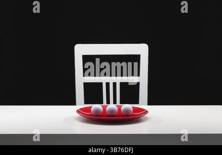 Three white golf balls on the red plate. White old chair and white table in the dark room Stock Photo