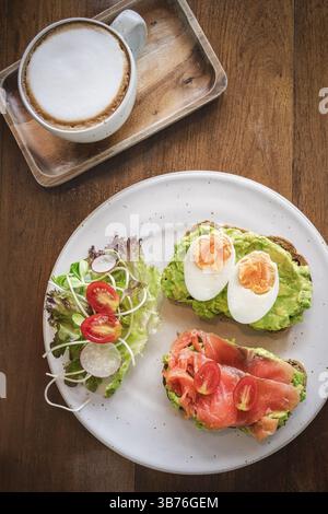 A vibrant breakfast spread includes two slices of toasted bread topped with creamy avocado, perfectly sliced smoked salmon, and halved soft-boiled egg Stock Photo
