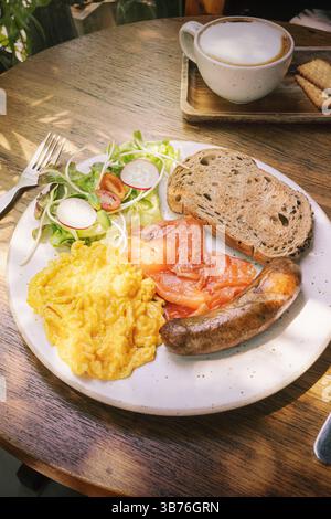 breakfast plate fluffy scrambled eggs, rich smoked salmon, a savory sausage, and a fresh salad with radishes and tomatoes, all complemented by slices Stock Photo