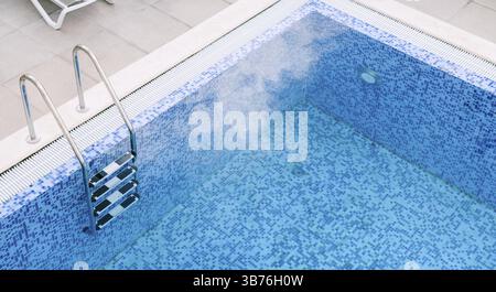A chrome staircase with railings in a pool with blue mosaic. Stock Photo