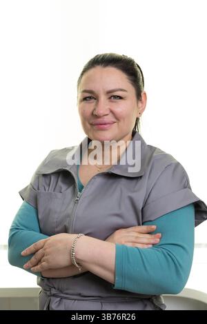 Portrait of a confident woman standing with her arms crossed, wearing a gray outfit, and smiling warmly while posed against a bright white background Stock Photo
