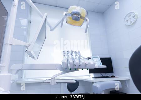 The image showcases a contemporary dental clinic featuring a dental chair, monitor, dental tools, and ambient lighting, emphasizing a clean and comfor Stock Photo