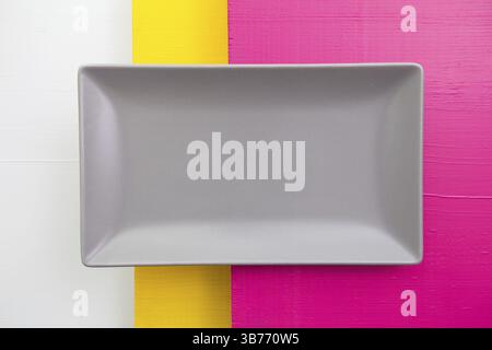Empty gray ceramic dish on over white, yellow and pink wooden table, rectangle dish Stock Photo