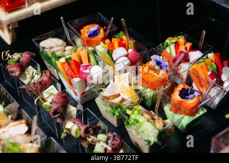 Colorful appetizer cups filled with fresh vegetables, salads, sushi rolls, and rolled meats, creatively presented with sauces and garnishes. Stock Photo