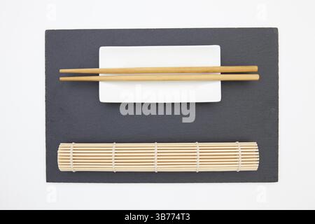 Rectangular slate plate with chopsticks, ceramic plate, bamboo mat for sushi on the white table Stock Photo
