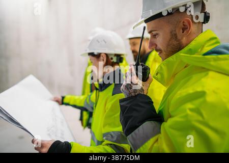 Team of engineers and construction workers reviewing blueprints, building site. Stock Photo