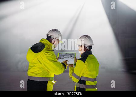 Engineers discussing construction plans using a tablet on site. Stock Photo