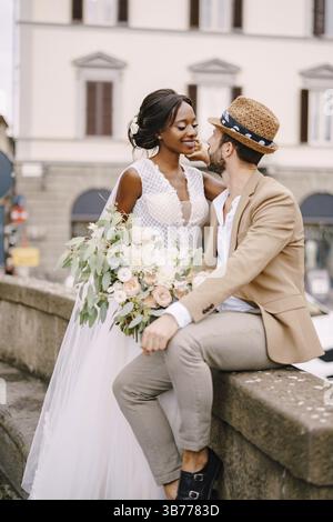 Wedding in Florence, Italy. Interracial wedding couple. African-American bride in a white dress with a long veil and a bouquet, and Caucasian groom in Stock Photo