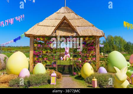 Vibrant garden scene featuring a decorative hut adorned with flowers, pastel eggs, and bunny figures, under a clear blue sky, perfect for Easter celeb Stock Photo