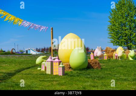Brightly colored Easter egg decorations in a vibrant park setting during spring, featuring large eggs, pastel houses, and festive bunting. Stock Photo