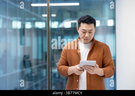 A focused programmer is seen thoughtfully interacting with a tablet device in a modern office setting. Stock Photo