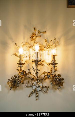 Gold three-lamp floor lamps, decorated with floral patterns on the wall. Interior details of an old villa in Italy. Stock Photo