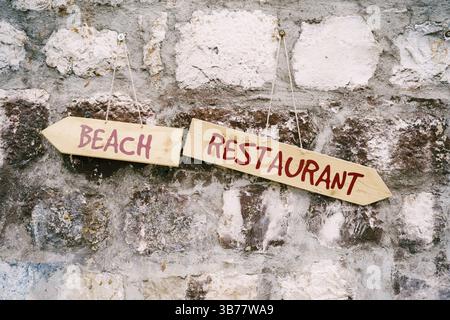Two multidirectional signs with inscriptions hang on a stone wall. Stock Photo