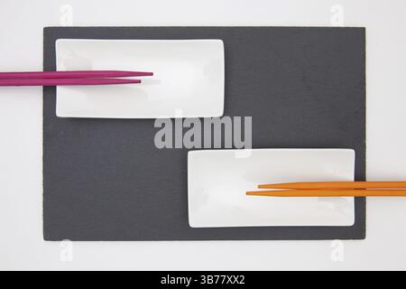 Rectangular slate plate with ceramic plate purple and orange chopsticks for sushi on the white table. Food Design Stock Photo