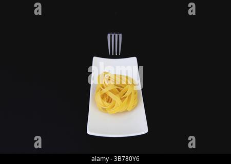 Stainless fork and tagliatelle pasta on the white plate. Diet lunch Stock Photo