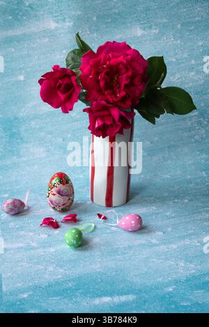 Easter and spring background with Easter eggs, vase and red roses on the blue background Stock Photo