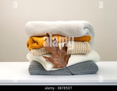 Stack of knitted clothes decorated with autumn leaf, woolen sweaters.Knitwear. Stock Photo
