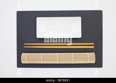 Rectangular slate plate with chopsticks, ceramic plate, bamboo mat for sushi on the white table. Food Design Stock Photo