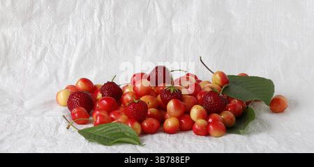 Ripe pink cherries and ripe strawberries lie on a white background. Stock Photo