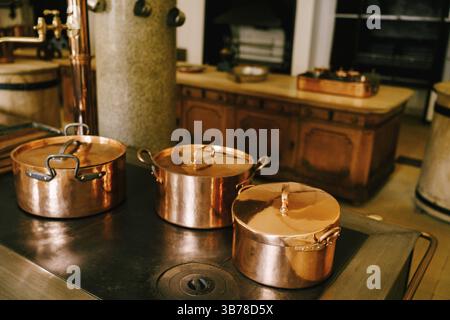 Three copper pots on the stove against the background of a long wooden table in a vintage dining room. Stock Photo