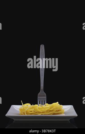 Stainless fork and tagliatelle pasta on the white plate in the dark room. Diet lunch Stock Photo