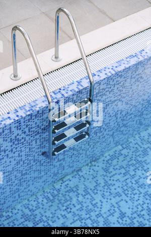 A close-up of the stairs in the pool, against a blue mosaic background. Stock Photo