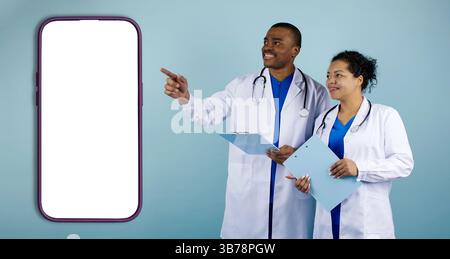 Medical Ad. Smiling Black Doctors In Uniform Pointing At Blank Smartphone Screen Stock Photo