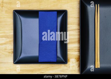 Black ceramic bowls and bamboo chopsticks for sushi food with dark blue napkin Stock Photo