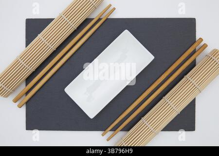 Rectangular slate plate with chopsticks, ceramic plate, bamboo mat for sushi on the white table Stock Photo