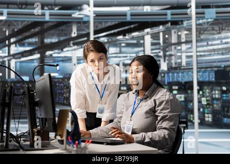 Manager overseeing work done by engineer in server hub, analyzing rigs data. Data center office team leader supervising employee examining supercomputers gear, ensuring system integrity and security Stock Photo
