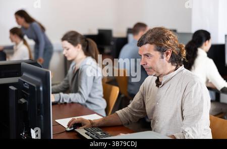 Man student of computer courses looks at monitor screen, types on keyboard and does work Stock Photo