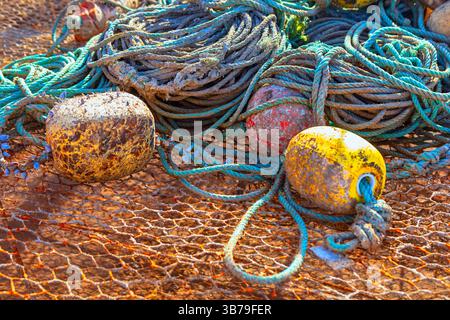 Tangled pile of weathered fishing ropes and nets, accompanied by worn, buoys in shades of yellow and brown. Scene captures  rugged, hardworking Stock Photo