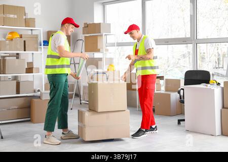 Male loaders wrapping boxes with stretch film in warehouse Stock Photo