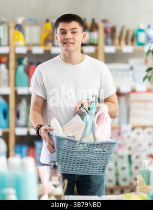 Guy selects various household cleaning products for cleaning the house with full basket of various purchases Stock Photo