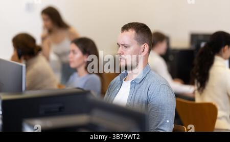 Guy student of computer courses looks at monitor screen, types on keyboard and does work Stock Photo