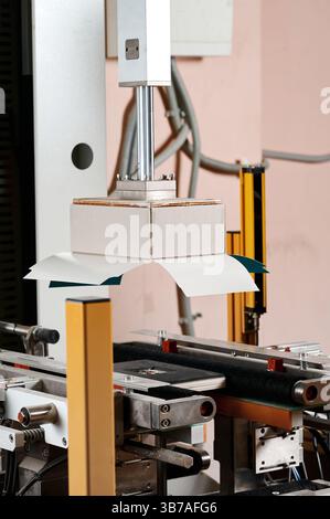 Innovative machine expertly wrapping rectangular boxes in a busy packaging facility during daylight hours Stock Photo