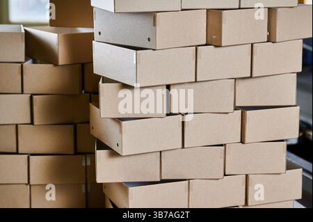 Stacked cardboard box blanks ready for assembly in a bustling manufacturing facility Stock Photo