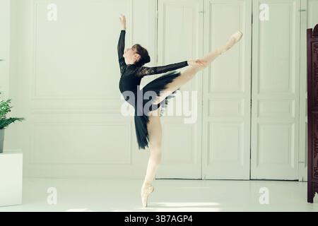 A young ballerina in a black tutu poses arabesque, total black, black swan Stock Photo