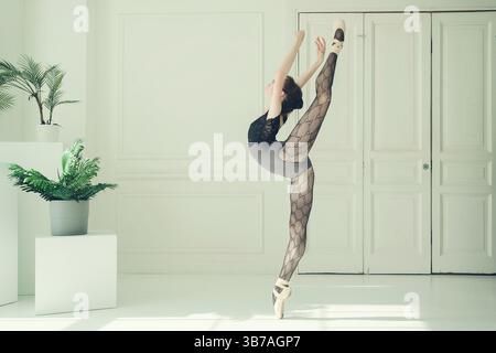 A young ballerina in leotard and lace tights poses performing vertical splits standing on pointe shoes Stock Photo