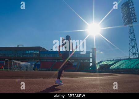 a female athlete runs on a treadmill at the stadium in the rays of the sun, the silhouette of a running athlete Stock Photo