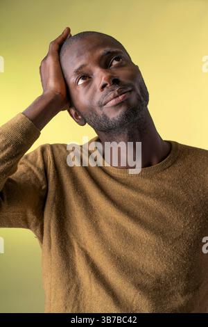 Close-up portrait of a thoughtful man touching his head while looking up, captured in studio on yellow background Stock Photo