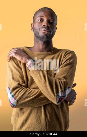 Portrait of a self-assured man crossing arms while looking at camera on yellow background Stock Photo