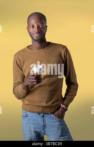 Confident young man enjoying coffee break with takeaway cup against yellow background Stock Photo