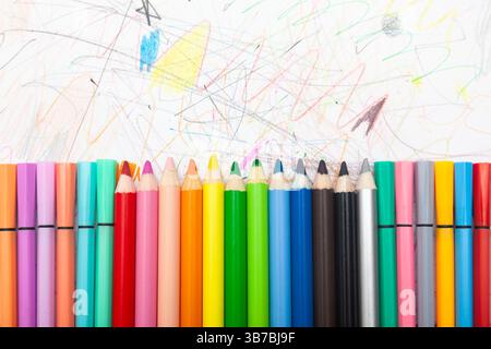 Multi-colored pencils lie on white paper drawn with multi-colored curved lines. Stock Photo